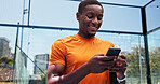 Man, phone and texting with smile at tennis court, fitness and scroll on break for chat at urban park. African person, low angle and smartphone on mobile app, social media and training at sports club