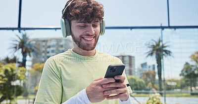 Buy stock photo Man, phone and headphones with fitness at tennis court, audio or smile on break for chat at urban park. Person, smartphone and listen to music on mobile app, streaming or happy at sports club in town