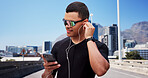 Man, runner and phone with earphones in city, sunglasses and smile with fitness, streaming and sound. Person, happy and smartphone with mobile app, audio or listen to music on bridge in urban town