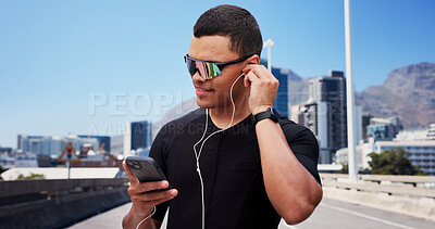 Buy stock photo Man, runner and phone with earphones in city, sunglasses and smile with fitness, streaming and sound. Person, happy and smartphone with mobile app, audio or listen to music on bridge in urban town