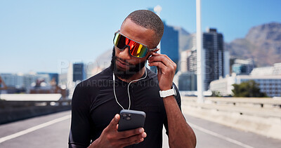 Buy stock photo Black man, runner and phone with earphones on bridge, sunglasses and exercise with streaming in city. Person, sound and smartphone with mobile app, click or listen to music for fitness in urban town