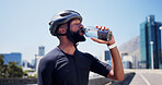 Black man, cyclist and drinking water in city, fitness and helmet on bridge, break and hydration in street. African person, bottle and rest with training, outdoor and liquid for electrolytes in town