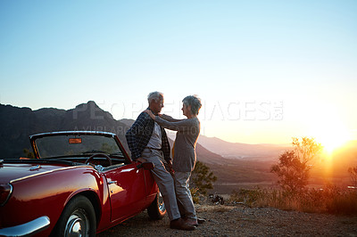 Buy stock photo Old couple, hug and car at sunset on road trip, mountains or space with sky, love and vacation. Elderly man, woman and embrace with convertible vehicle, outdoor and travel on holiday in retirement