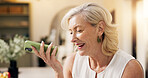 Senior, happy woman and talking with speaker phone in home for communication or friendly discussion. Female person, smile or mobile smartphone with loudspeaker for call, audio message or voice note