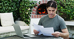 Man, finance and laptop with documents for expenses, mortgage bills or payments by fireplace. Male person, reading and computer with paperwork or invoice for financial planning, audit or budget check