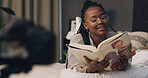 Black woman, influencer and reading book in bedroom for content creation, glasses or literature for children. African person, happy and online tutorial on social media, story or recording at house