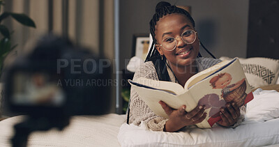 Buy stock photo Black woman, influencer and reading book in home for content creation, camera or literature for children. African person, happy and online tutorial on social media, story or recording on bed at house