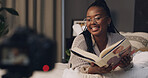 Woman, influencer and reading book with smile for content creation, camera or literature for children. African person, happy and online tutorial on social media, story or recording on bed at house