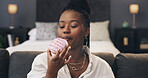 Black woman, relax and eating donut on sofa in home, sweet snack and junk food on break in bedroom. African person, pastry or dessert on couch for sugar craving, cake and cheat meal at apartment