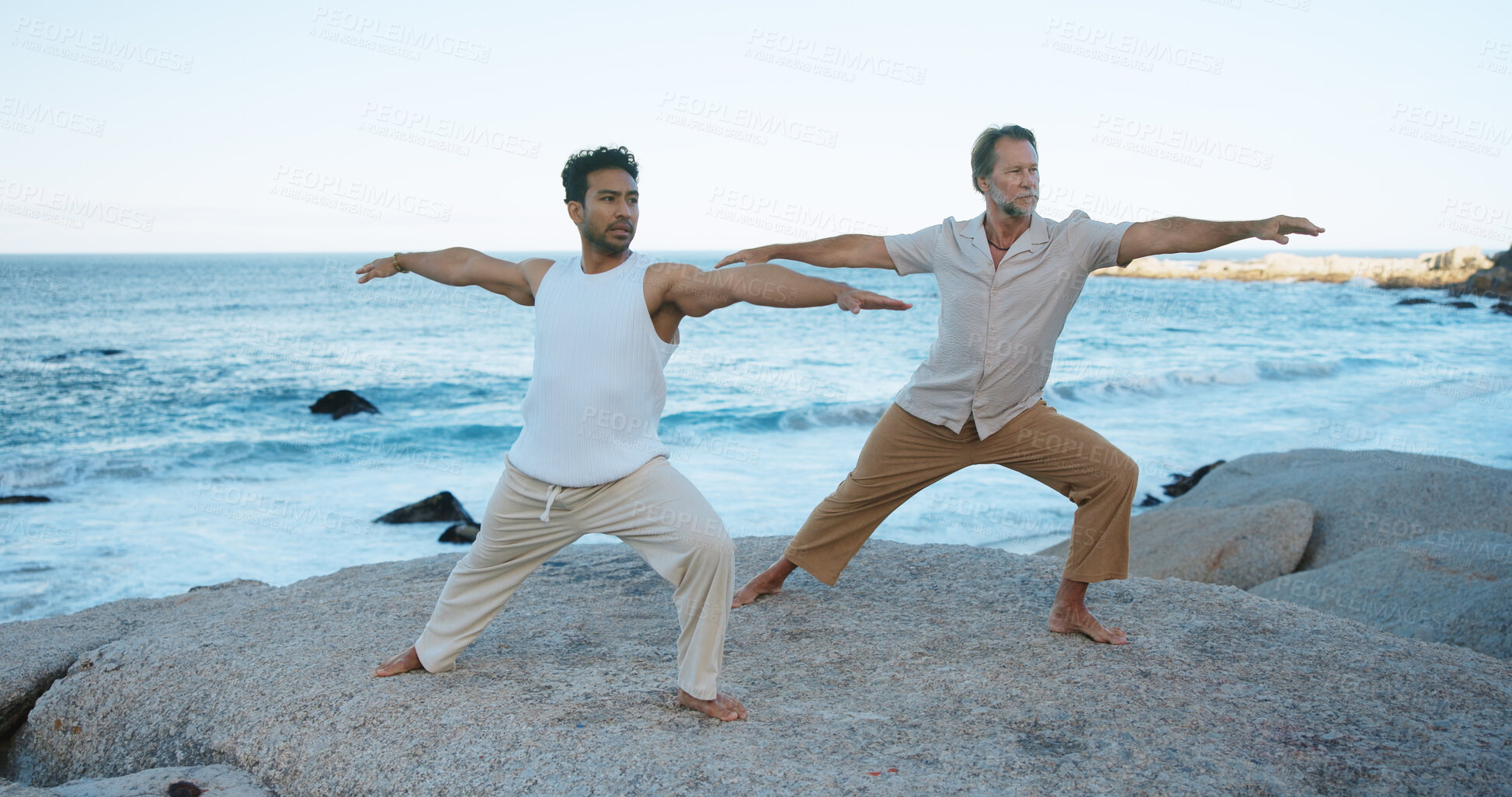 Buy stock photo Fitness, men and stretching at beach with yoga outdoor, holistic health and balance for wellness. Active, people and warrior pose at ocean with stability, coordination and exercise for stress relief.