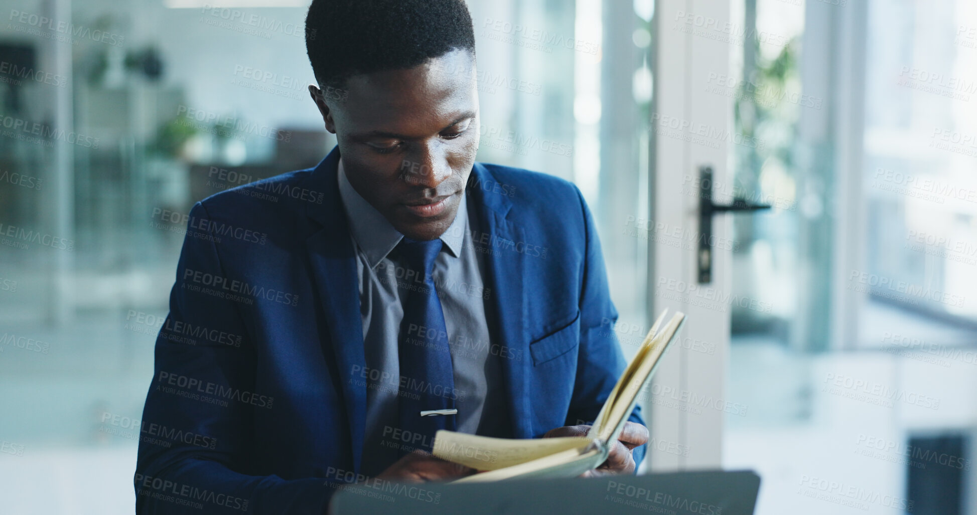 Buy stock photo Black man, lawyer and reading notebook in office for research, case notes and trial reminder. Attorney, laptop and diary with legal agenda, review evidence and witness statement for court testimonial