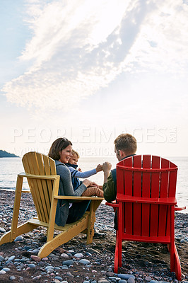 Buy stock photo Happy, chairs and parents with kid on beach for holiday, vacation and weekend getaway outdoor. Travel, family and mom, dad and child for bonding, relationship and relax by ocean, sea and nature