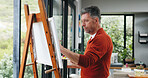 Mature man, painter and canvas with easel for art, drawing or creative sketching in home. Male person, artistic or painting with brush or color palette for artwork, creativity or talent in house