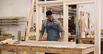 Carpenter, man and woodwork in workshop with timber, sandpaper or project for furniture manufacturing. Woodworker, black person and artisan in factory with carpentry equipment, PPE and craftsmanship.