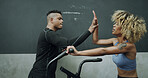 Woman, personal trainer and high five with bike at gym for fitness, exercise and cycling success. Tired, female person and coach with bicycle for celebration, training achievement and wellness goals