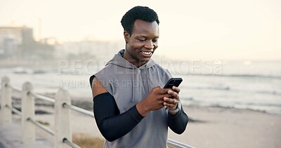 Buy stock photo Black man, phone and happy at beach with fitness app on promenade, scroll and monitor for training. African person, runner and smile with smartphone, notification and space for exercise by ocean