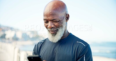 Buy stock photo Old man, smile and fitness by beach with phone, social media post or notification for wellness app. Senior black person, workout rest and tech on promenade outdoor with text, website and online chat.