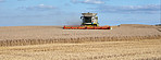 Harvester, machine and farming with crops in nature for agriculture, cutting wheat and collection. Blue sky, vehicle and equipment for farm fields, food production and harvesting season of plantation