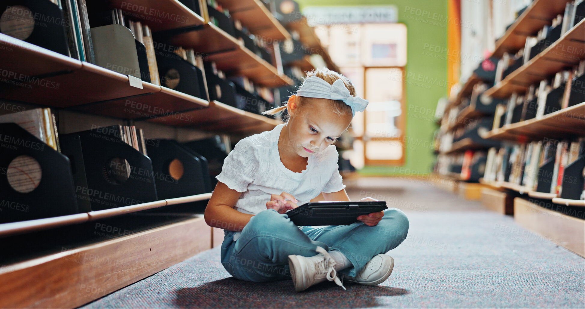 Buy stock photo Girl, child and reading in library with tablet, ebook website and online literature for development. Kid, scroll and browsing at school with tech, storytelling app and education for knowledge growth.