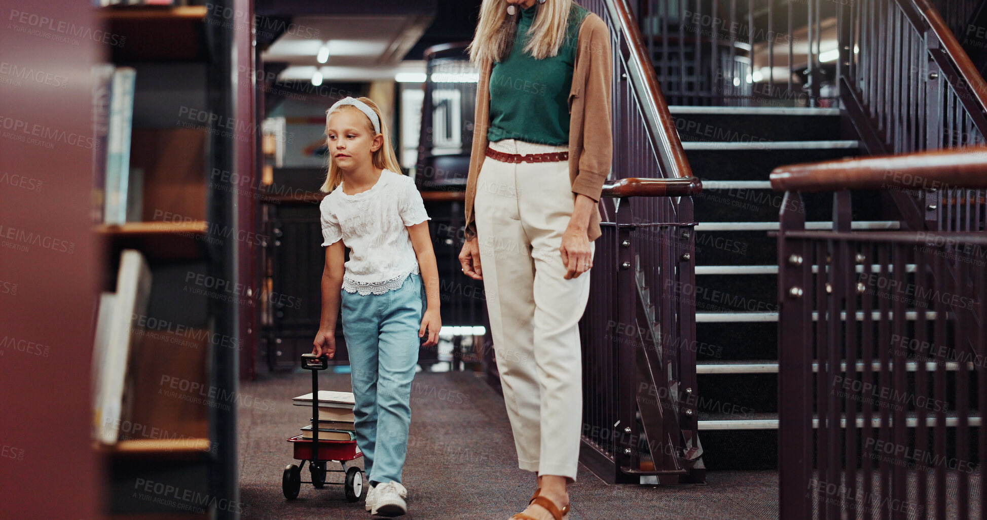 Buy stock photo Mother, child and book cart in library, browsing novel selection and collect literature for knowledge. Walking, learning resources and woman with girl in bookstore, parent support and study material