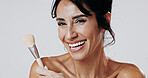 Woman, makeup brush and smile in studio portrait for beauty, powder and confidence on white background. Mature person, cosmetics and tools for facial foundation, blush and happy in New Zealand