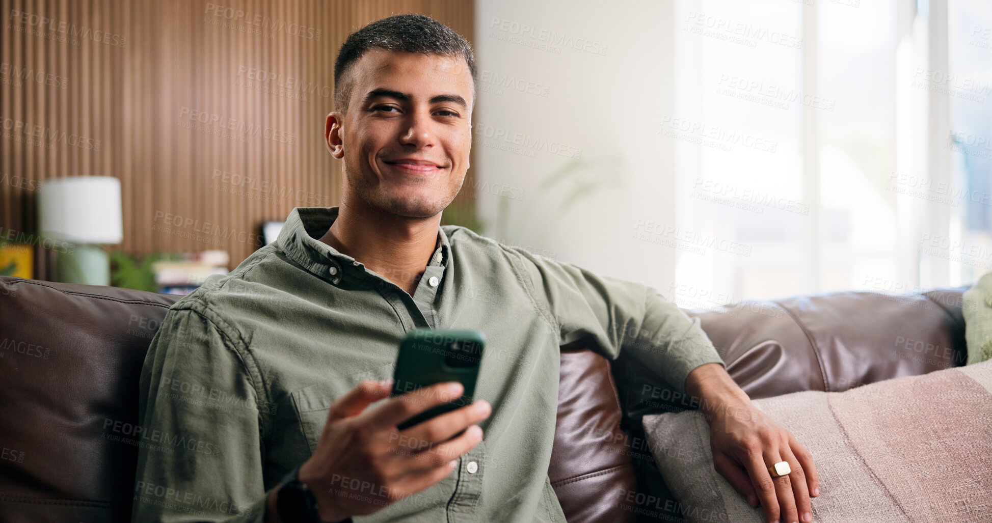 Buy stock photo Man, phone and relax with smile on couch in home for texting, web chat or online dating in lounge. Person, smartphone and happy in portrait, contact or social network on sofa at apartment in Mexico
