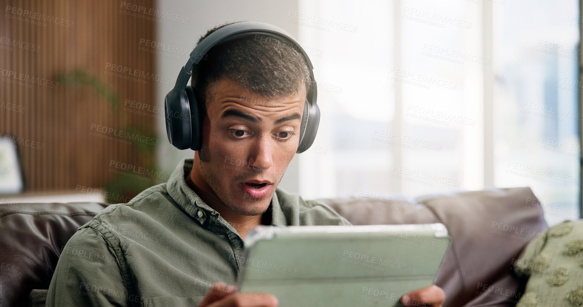 Buy stock photo Shock, tablet and man on sofa with headphones for online videos, subscription and watching movies. Home, reaction and person on digital tech for internet, website and streaming drama show on weekend