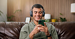 Man, phone and smile with headphones on sofa for streaming, relax and sound in living room at house. Person, smartphone and listen to music with subscription, mobile app or texting on couch in home