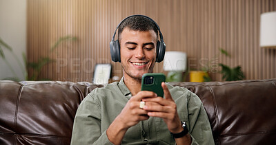 Buy stock photo Man, phone and smile with headphones on sofa for streaming, relax and sound in living room at house. Person, smartphone and listen to music with subscription, mobile app or texting on couch in home