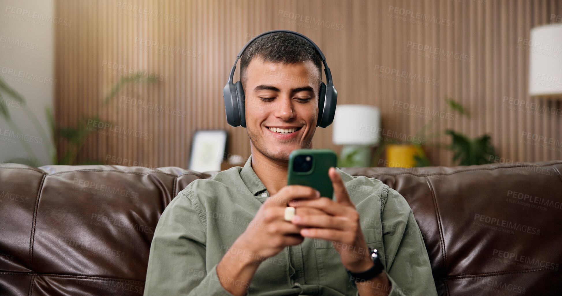 Buy stock photo Man, phone and smile with headphones on sofa for streaming, relax and sound in living room at house. Person, smartphone and listen to music with subscription, mobile app or texting on couch in home