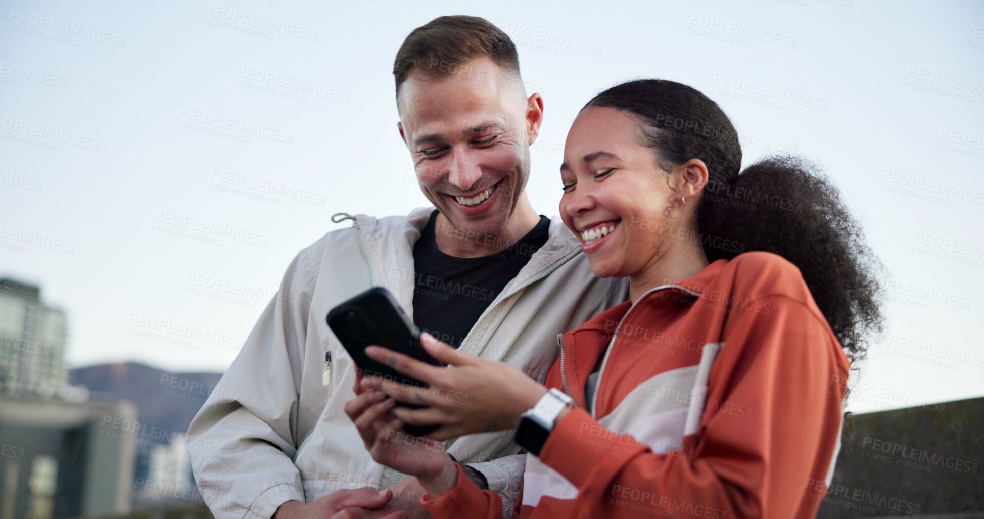 Buy stock photo Happy couple, fitness and phone with break in city for meme, notification or share post on bridge. People, runner and smartphone with app, smile or interracial relationship for exercise in urban town