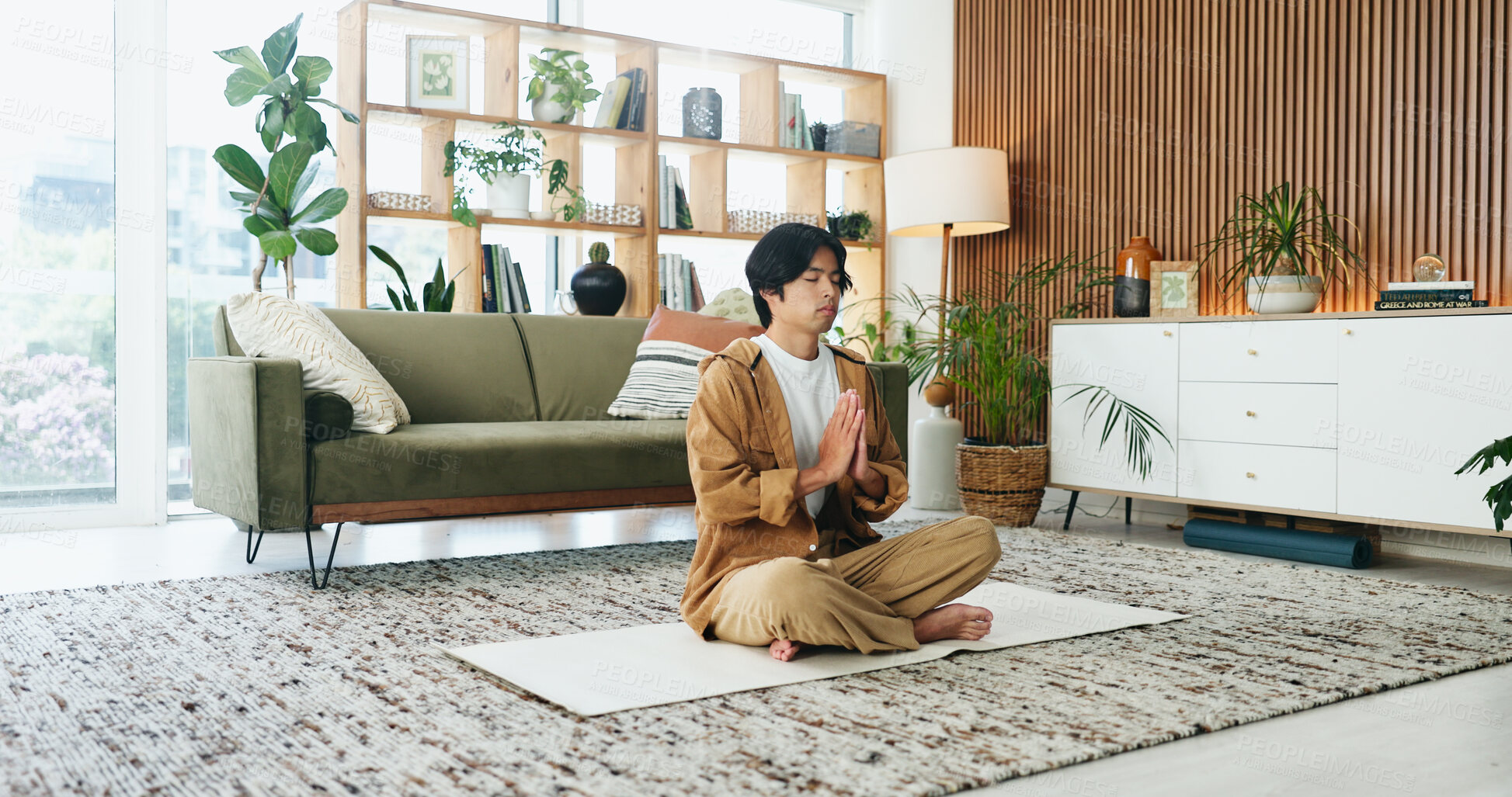 Buy stock photo Calm, man and meditation with prayer in lounge, mindfulness and zen with spiritual awareness in home. Person, wellness and self care for mental health on break, relax or healing with yoga and balance