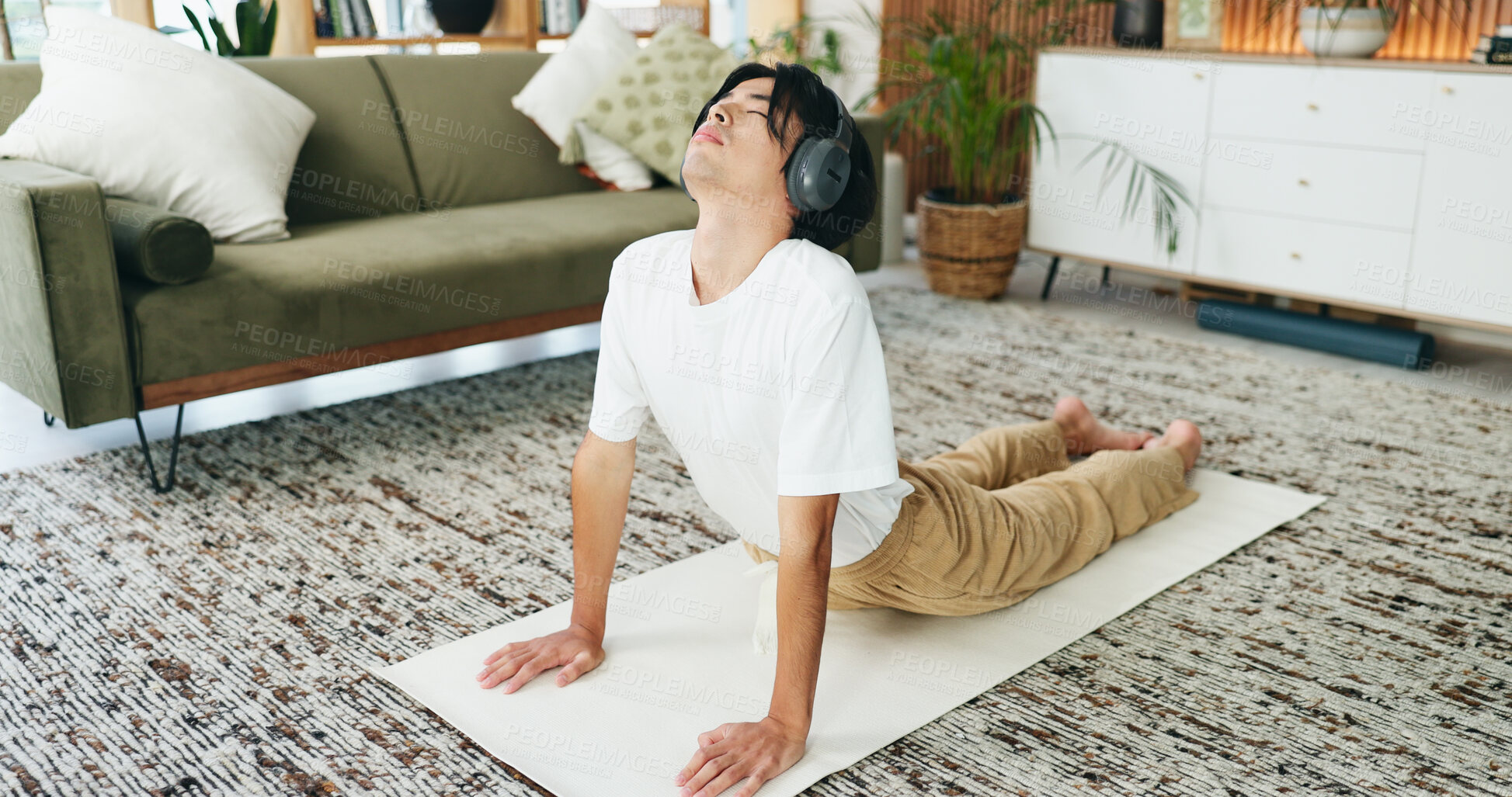 Buy stock photo Music, stretching and yoga with Asian man in home living room for exercise or wellness routine. Fitness, headphones and health with yogi person in cobra pose on floor for balance or holistic activity