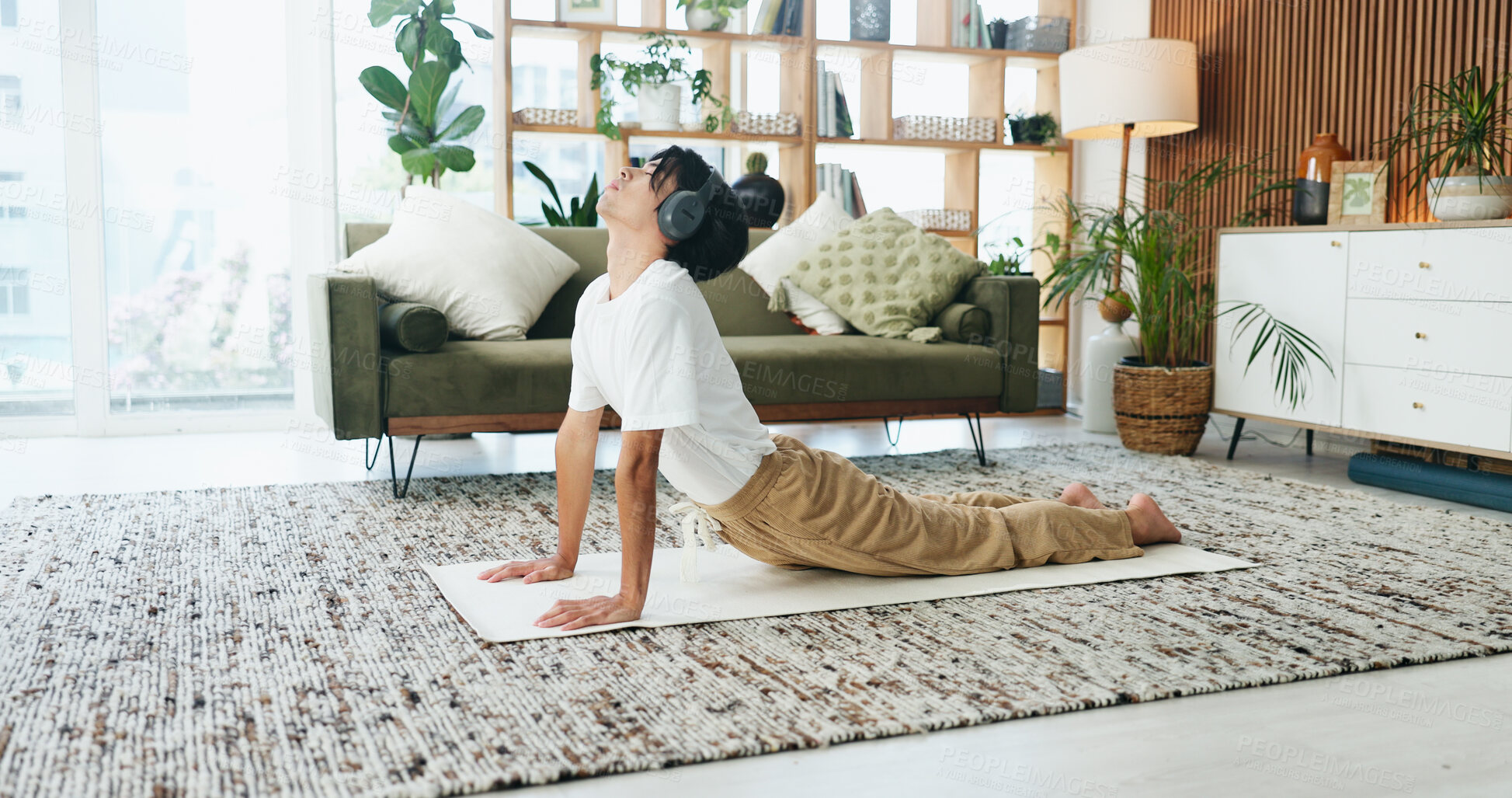 Buy stock photo Headphones, stretching and yoga with man on floor in home living room for exercise or wellness routine. Fitness, health and music with Asian person in cobra pose for balance or holistic activity