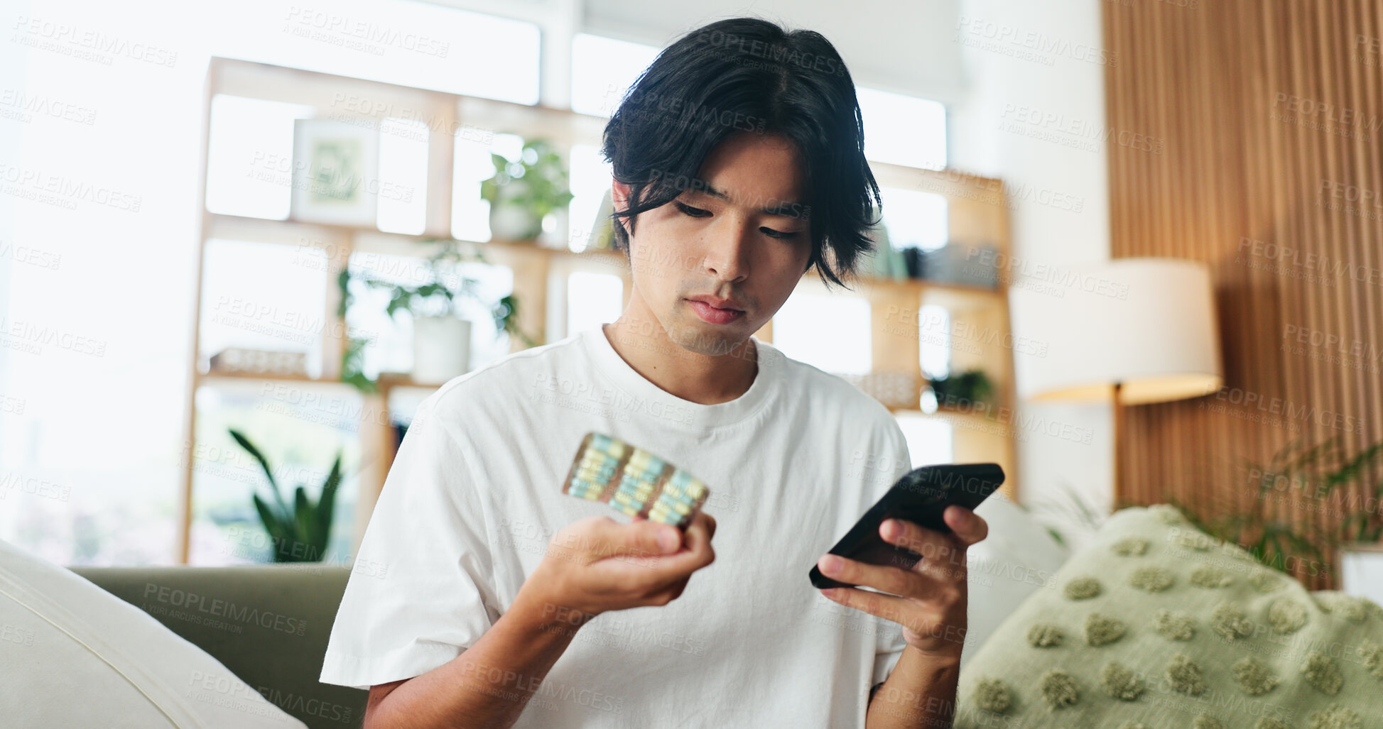 Buy stock photo Phone, pills and man in home for research, healthcare information or reading label for dose. Mobile, drugs and Asian person in house for medical prescription, medicine benefits or side effects