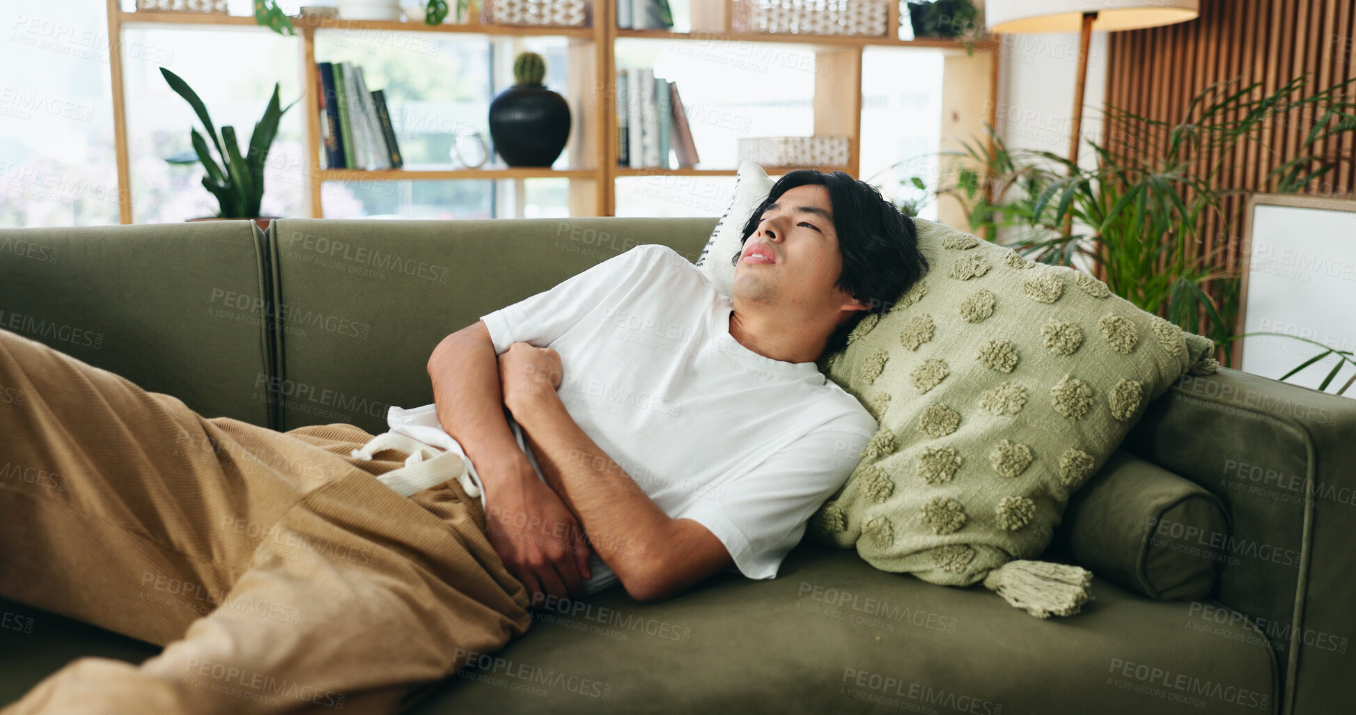 Buy stock photo Couch, discomfort and man with stomach pain in home, indigestion or food poisoning for gastro cramps. Sore tummy, bowel emergency or asian person with ibs condition for ache, constipation or diarrhea