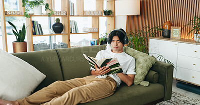 Buy stock photo Relax, headphones or man reading book on couch, emotional wellness guide or streaming author podcast. Home, Asian person or audio tech for ambient playlist, subscription service or literature for zen