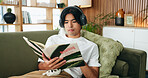 Relax, headphones or man reading book on sofa, emotional wellness guide or streaming author podcast. Home, Asian person or audio tech for ambient playlist, subscription service or literature for zen