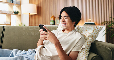 Buy stock photo Texting, laugh or Asian man on sofa with phone, online chat or communication on dating site. Happy, conversation or person in house with tech, digital app or connection on matchmaking platform.