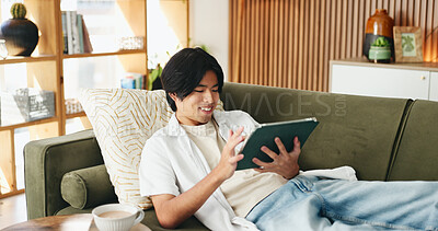 Buy stock photo Education, smile and tablet with Asian man on sofa in home living room for distance learning. App, online study and streaming with happy university student in apartment for development or growth