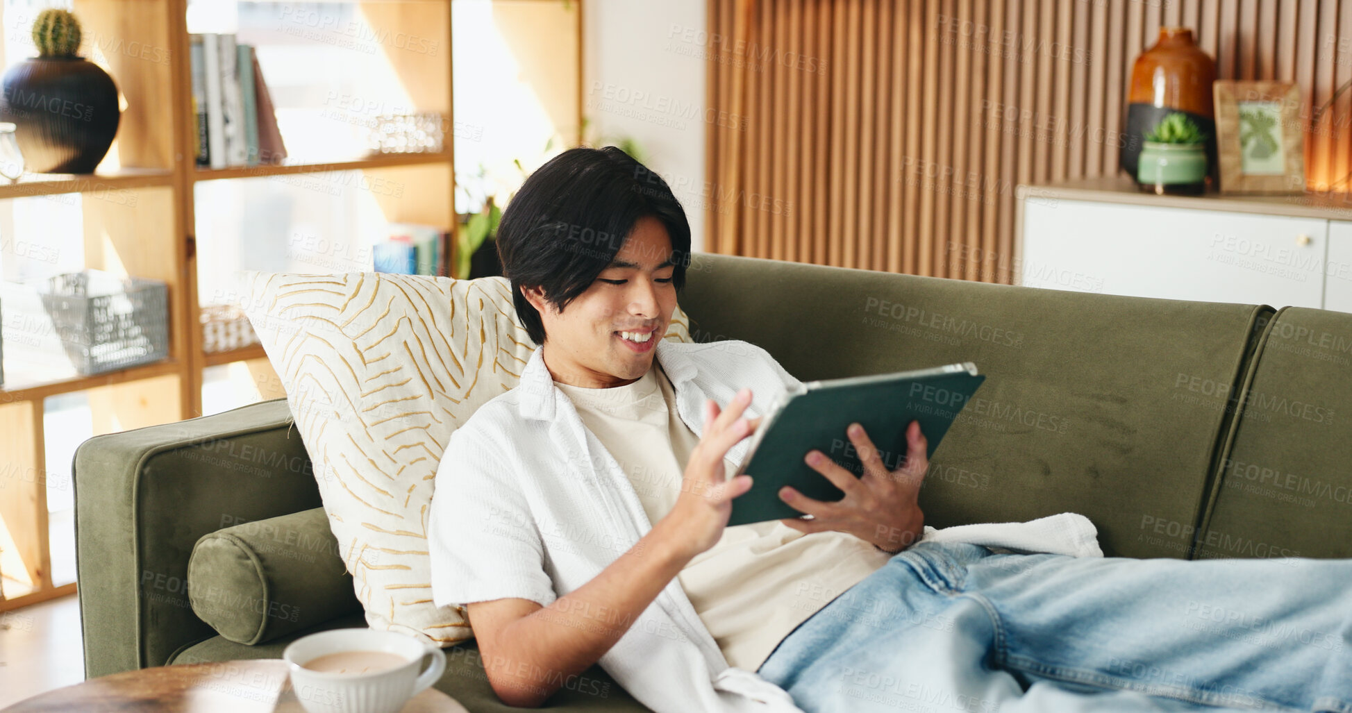 Buy stock photo Education, smile and tablet with Asian man on sofa in home living room for distance learning. App, online study and streaming with happy university student in apartment for development or growth