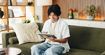 Buy stock photo Education, smile and tablet with man on sofa in home living room for distance learning or scrolling. App, online study and streaming with happy Asian student in apartment for development or growth