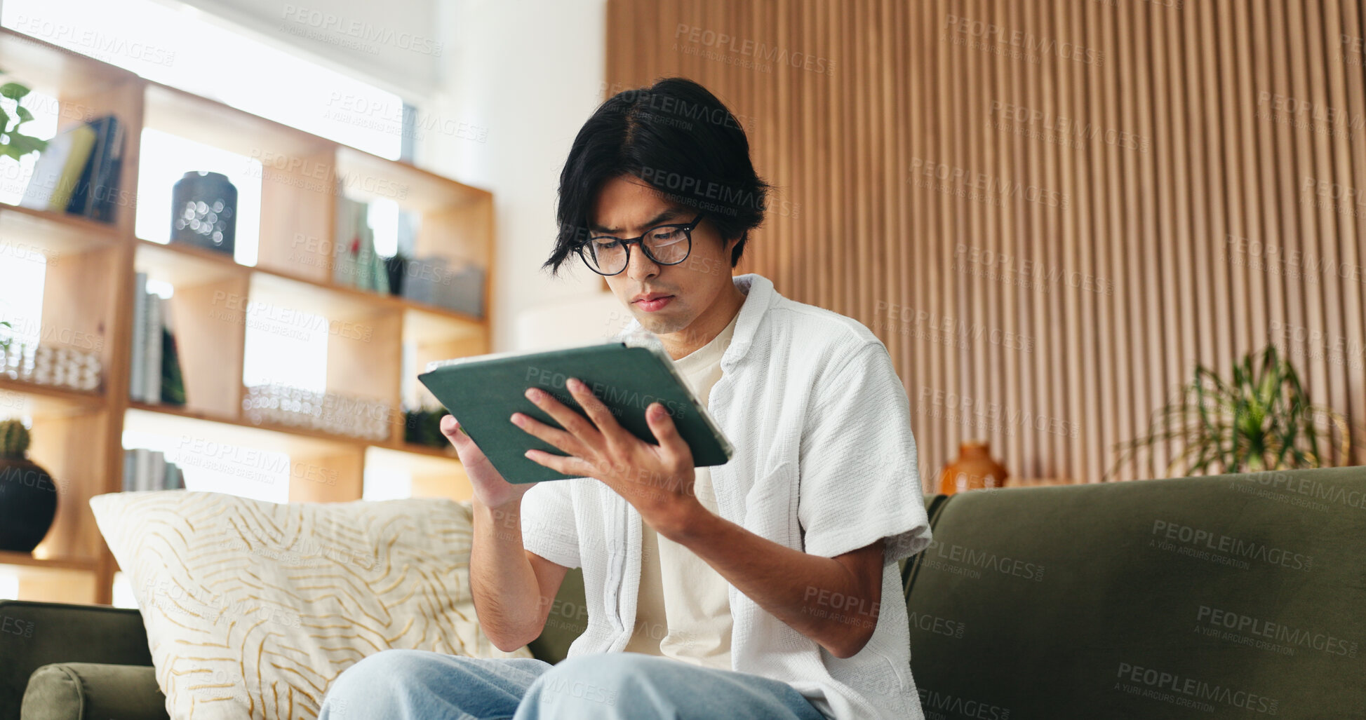 Buy stock photo Glasses, study and tablet with Asian man on sofa in home living room for distance learning. App, eyewear and online education with university student in apartment for development or streaming