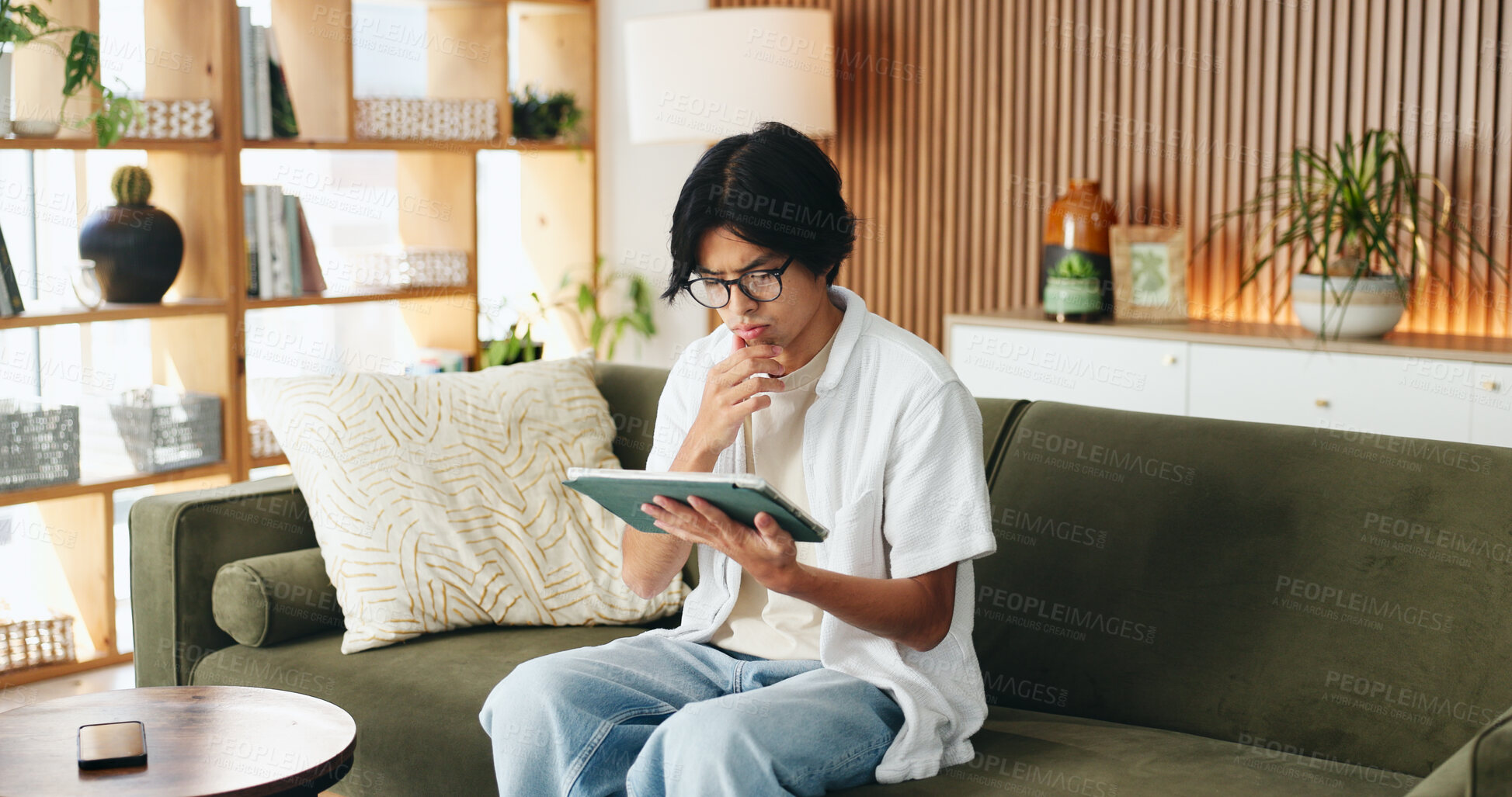 Buy stock photo Education, tablet and thinking with Asian man on sofa in home living room for distance learning. App, ideas and online study with thoughtful university student in apartment for development or growth