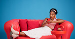 Phone, studio and wow with black woman on sofa for social media browsing, post or search. App, reaction and surprise with African person in shock on blue background for text message or typing