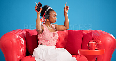 Buy stock photo Dance, headphones and studio with black woman on sofa for break, energy or radio streaming. App, music and phone with happy African person listening to song on blue background for satisfaction