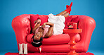 Music, phone and studio with black woman on sofa for audio streaming, break or satisfaction. App, headphones and laughing with happy African person listening to song on blue background for wellness