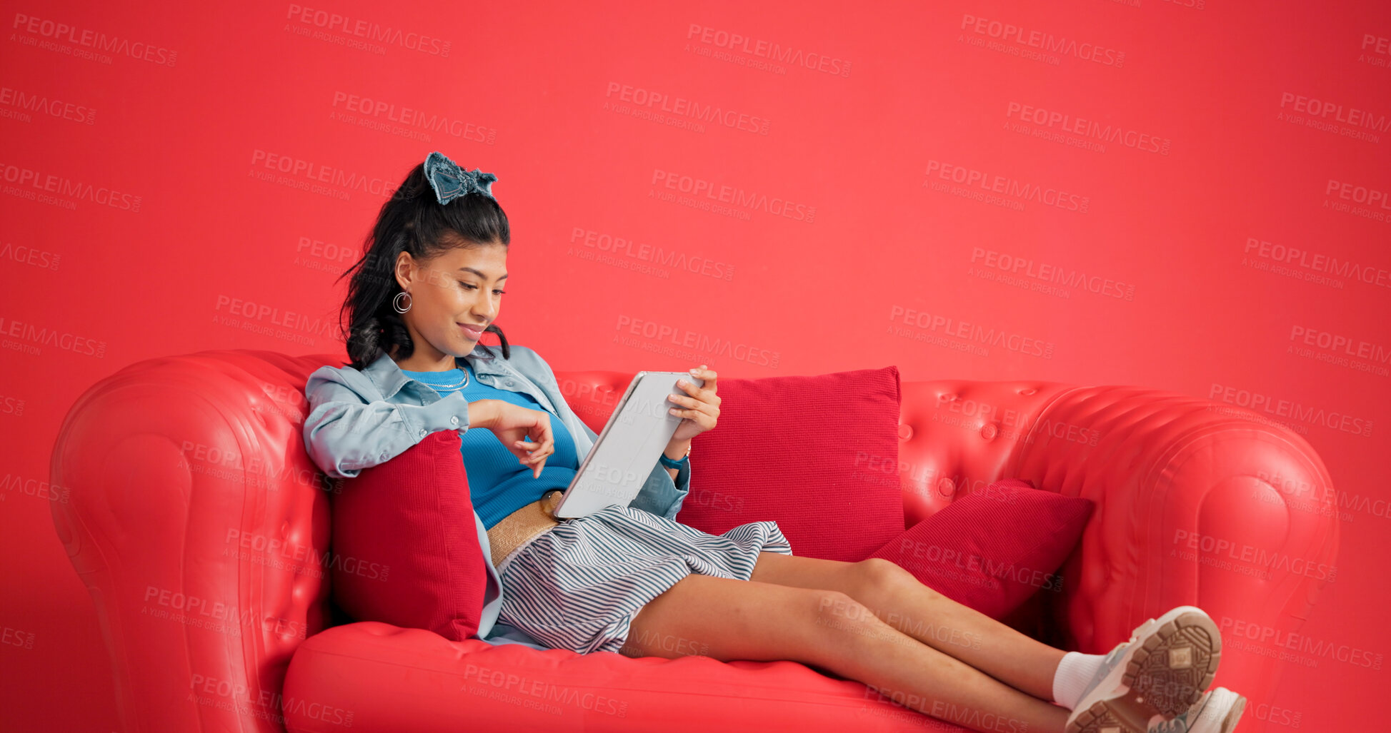 Buy stock photo Tablet, relax and woman on sofa in studio with networking, social media or connectivity on mobile app. Smile, calm and female person reading blog online with digital technology by red background.