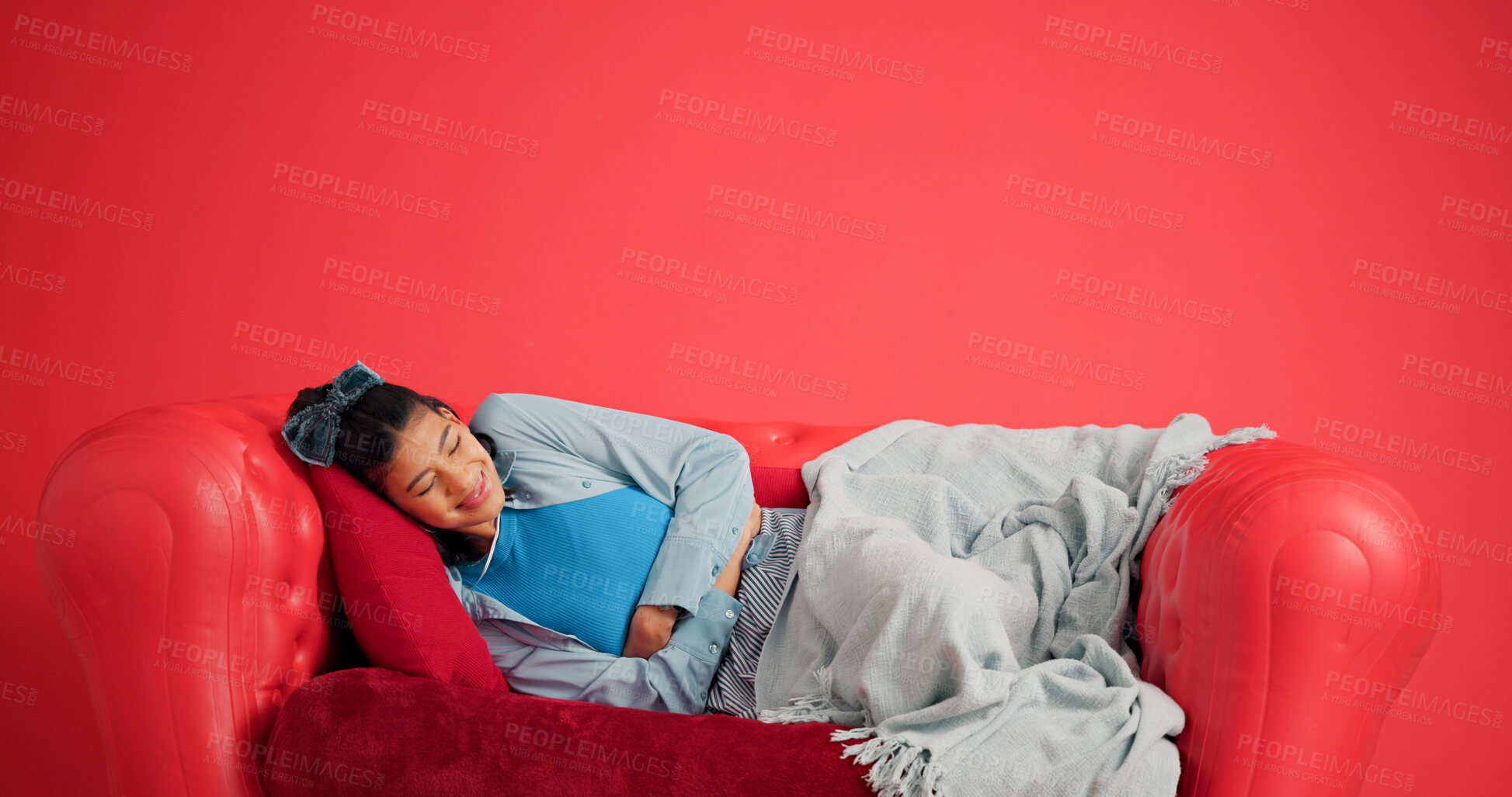 Buy stock photo Studio, woman and stomach ache on sofa, pain or period cramps on red background with mockup space. Sore abdomen, constipation and person with indigestion, sick or endometriosis with menstrual cycle