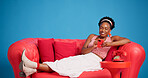 Phone, smile and studio with black woman on sofa for social media browsing, post or search. App, relax and typing with happy African person on blue background for download or mobile connection